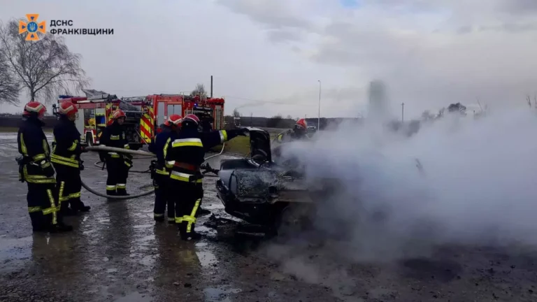 Пожежники гасять палаючу машину на дорозі.