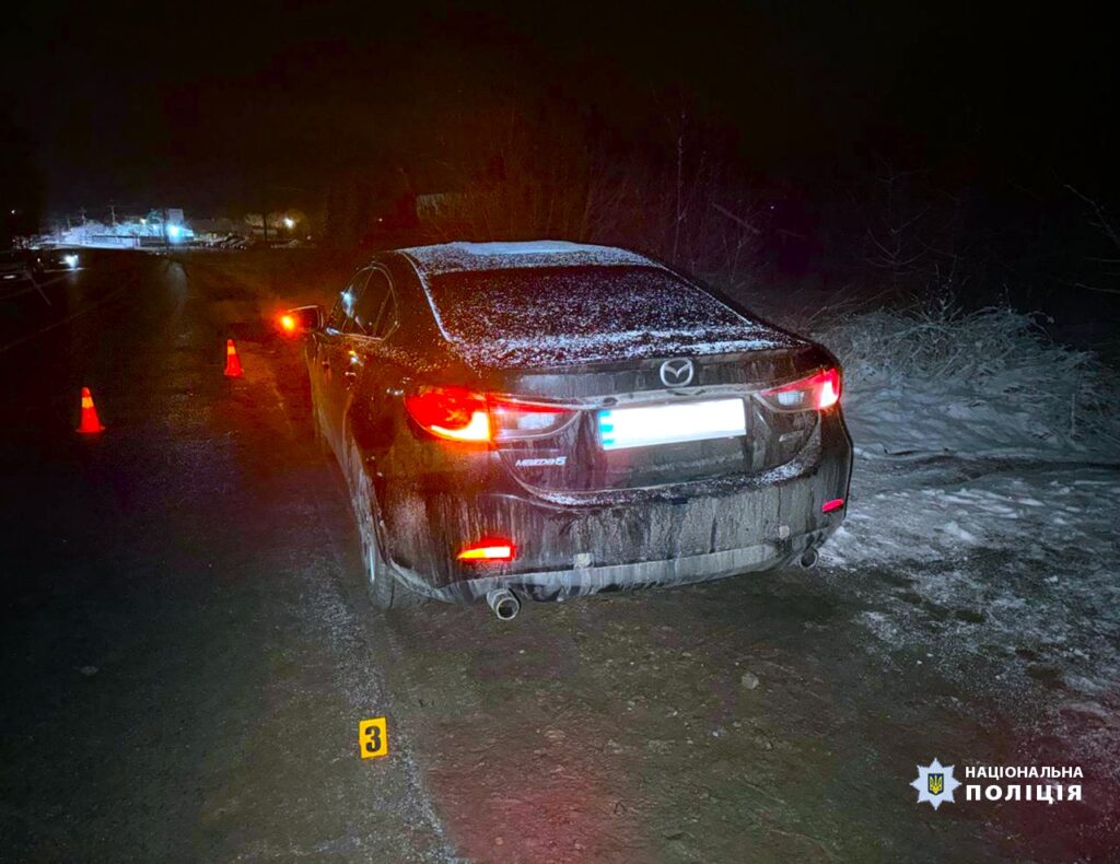 Машина на засніженій дорозі вночі з конусами.