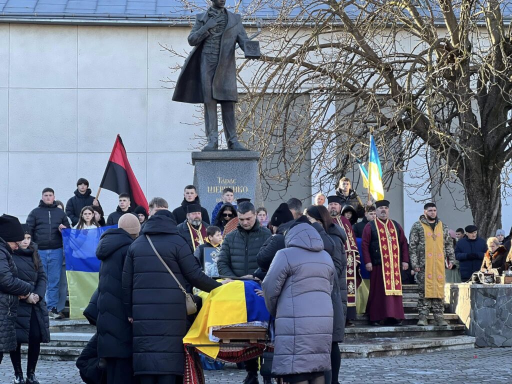 Церемонія біля пам'ятника з прапорами та людьми.