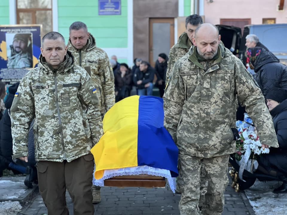 Військові несуть труну, покриту українським прапором.