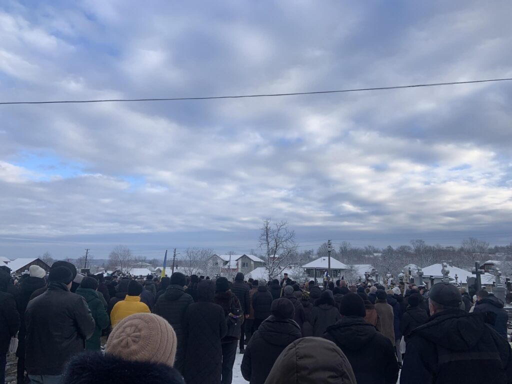 Зимовий натовп на цвинтарі під сірим небом.