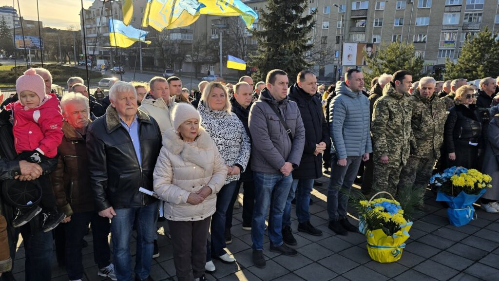 Люди на вулиці з українськими прапорами та квітами.