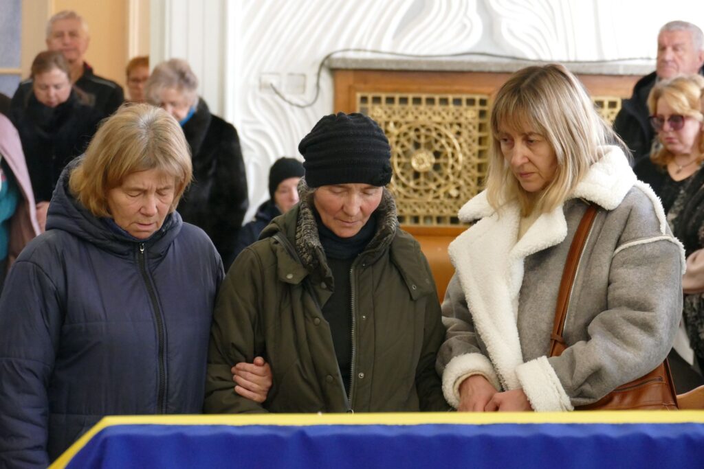 Люди на церемонії прощання, стоять біля труни.