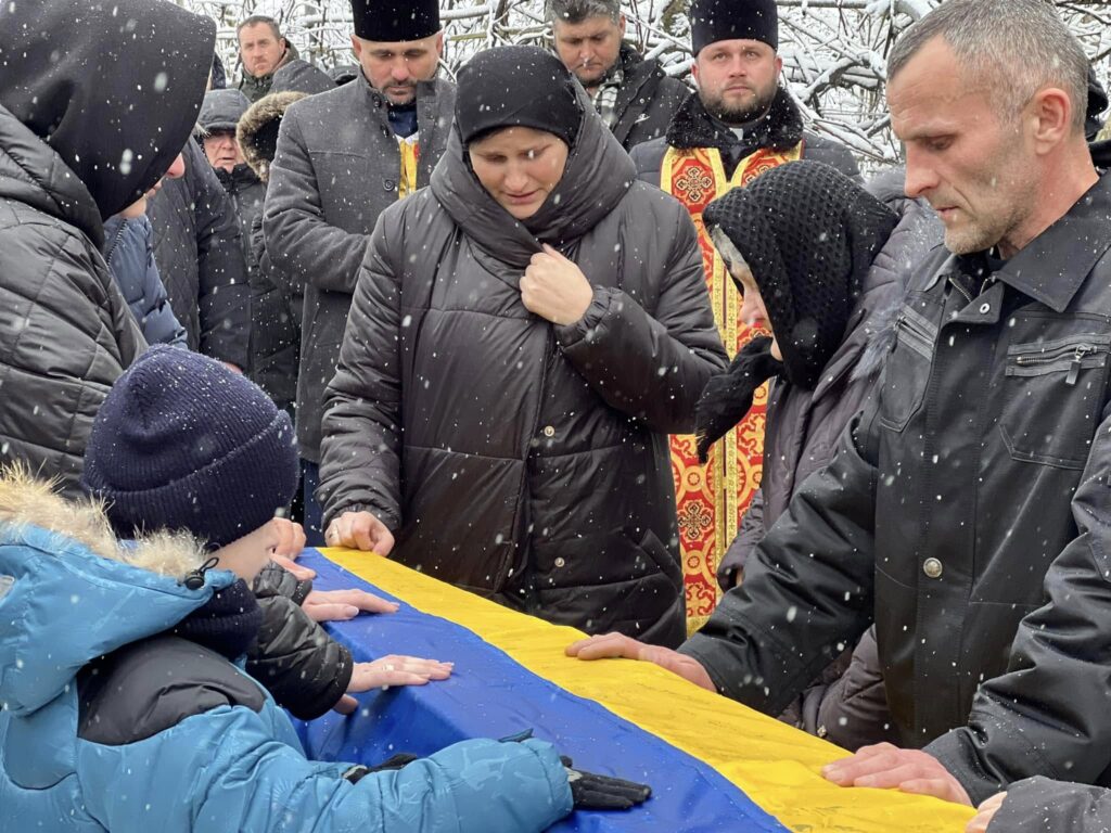 Люди прощаються біля труни з прапором України.