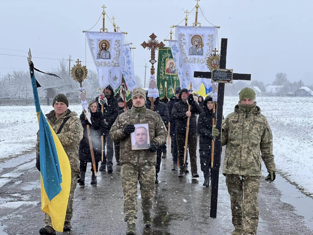 Похоронна процесія на снігу з прапорами України.