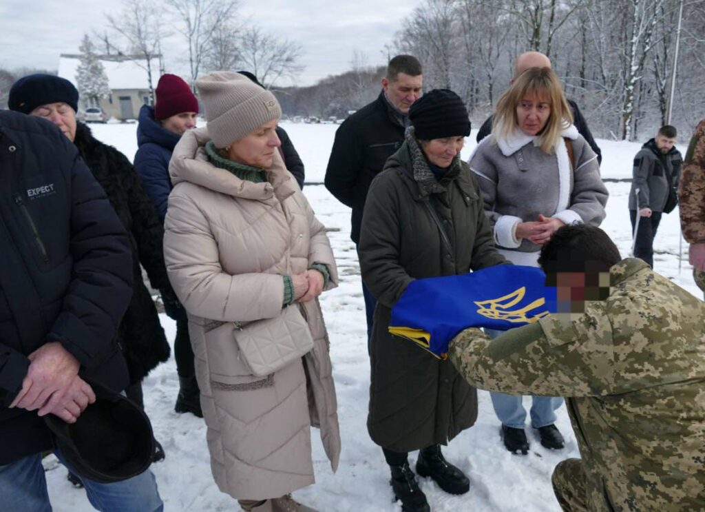 Люди на церемонії з українським прапором взимку.