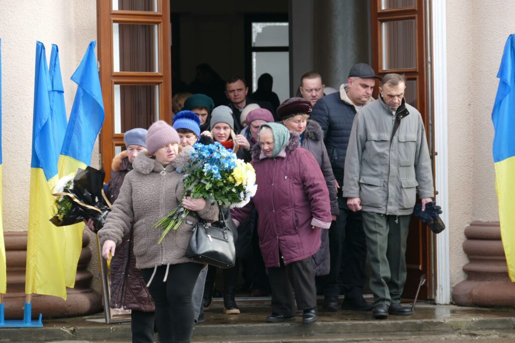 Люди виходять з будівлі, тримаючи квіти.