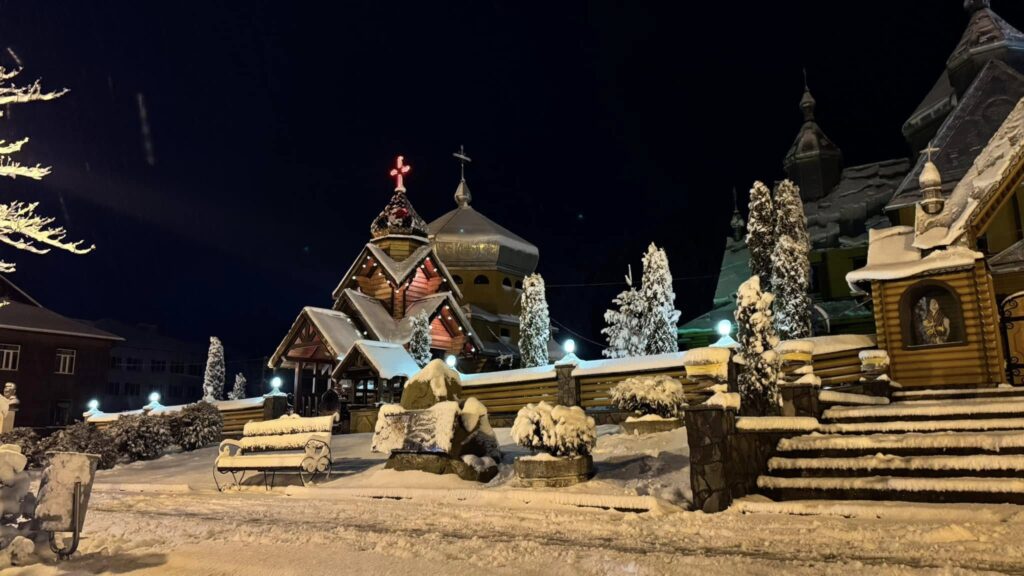 Засніжена церква вночі, освітлена ліхтарями.