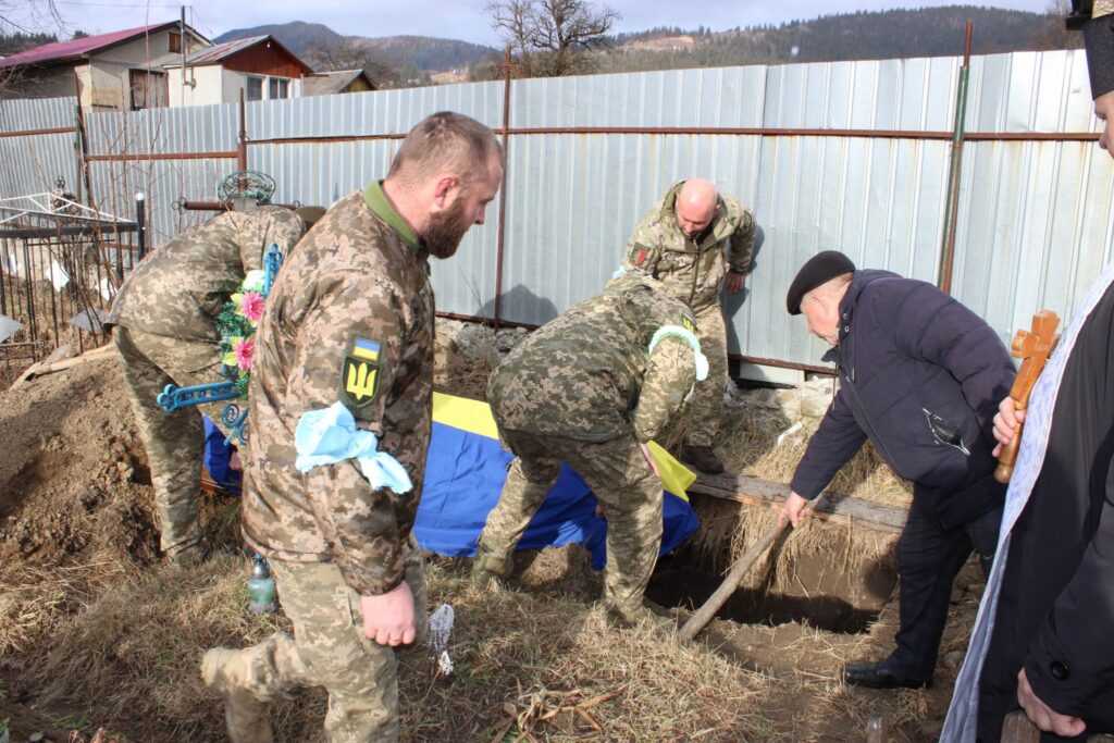 Військові ховають труну, вкрита прапором України.