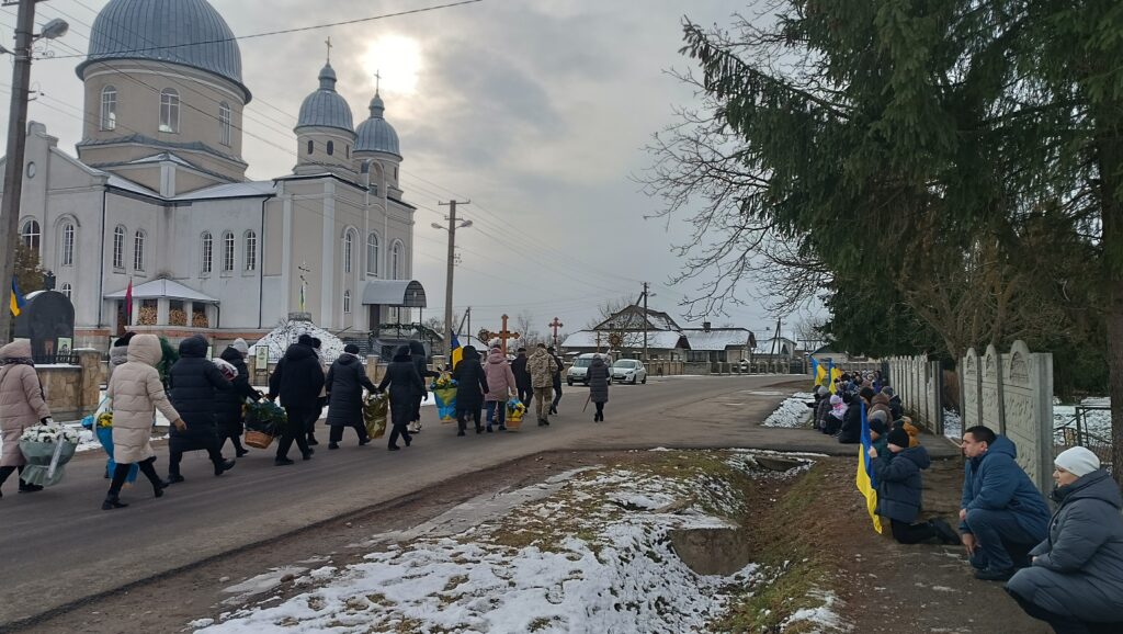 Люди на вулиці біля церкви з українськими прапорами.