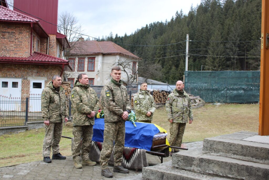 Військові несуть труну, вкриту прапором України.