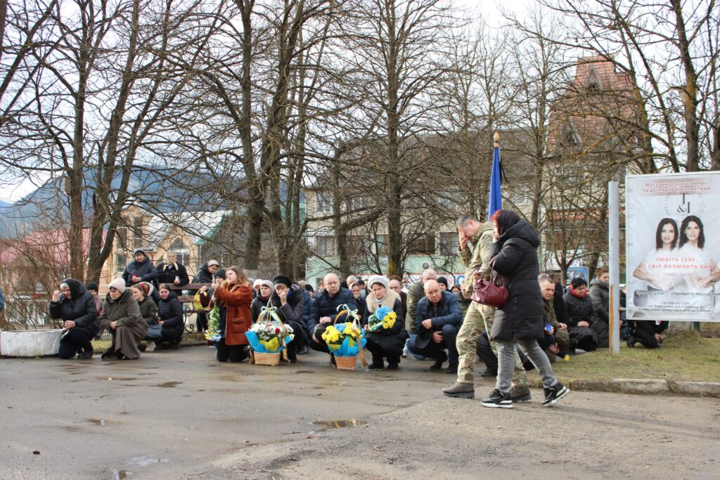 Люди на колінах з жовто-блакитними квітами на вулиці.