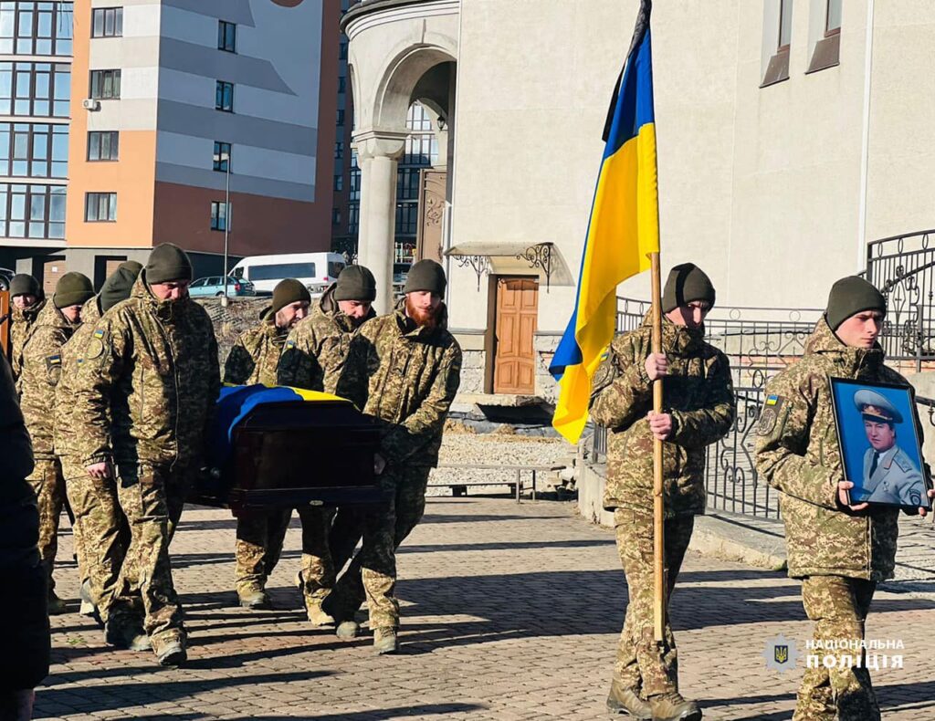 Військові несуть труну та прапор України.