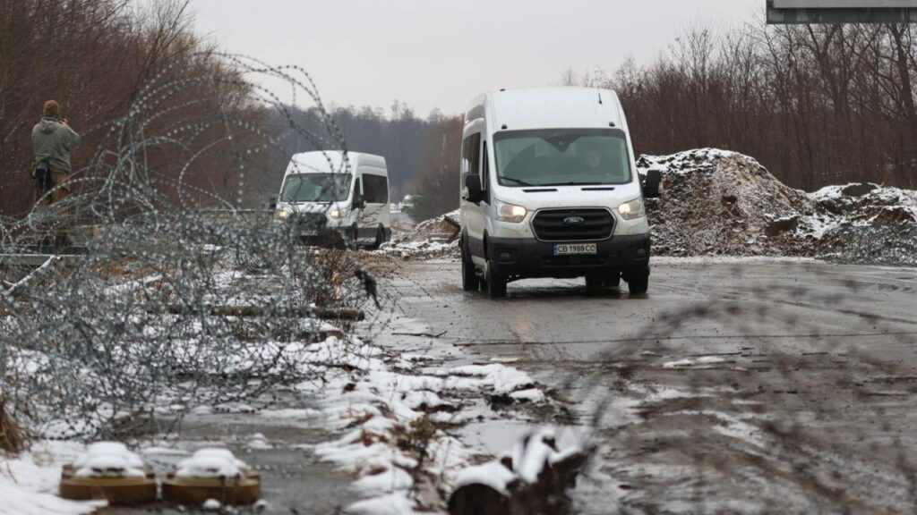 Фургони на сніжній дорозі, огородженій колючим дротом.