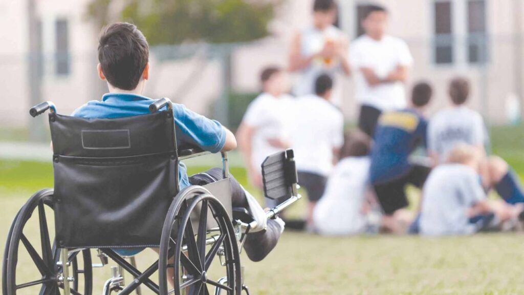 Хлопець у візку спостерігає за грою дітей.