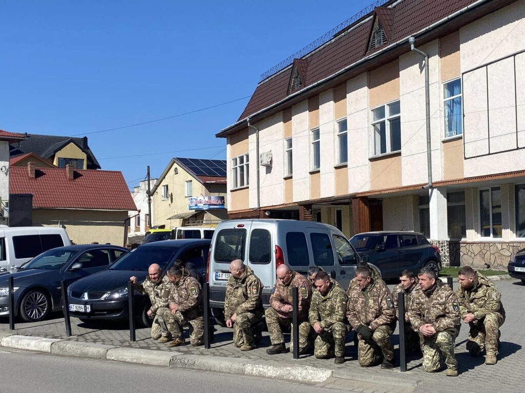 Військові на колінах перед будинком на вулиці.