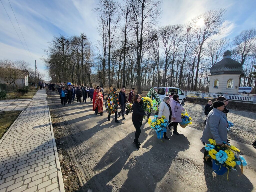 Похоронна процесія з вінками в селі взимку.