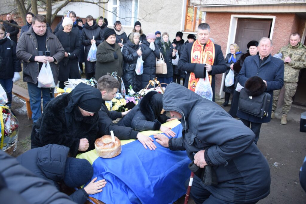 Люди прощаються з військовим, покритим українським прапором.