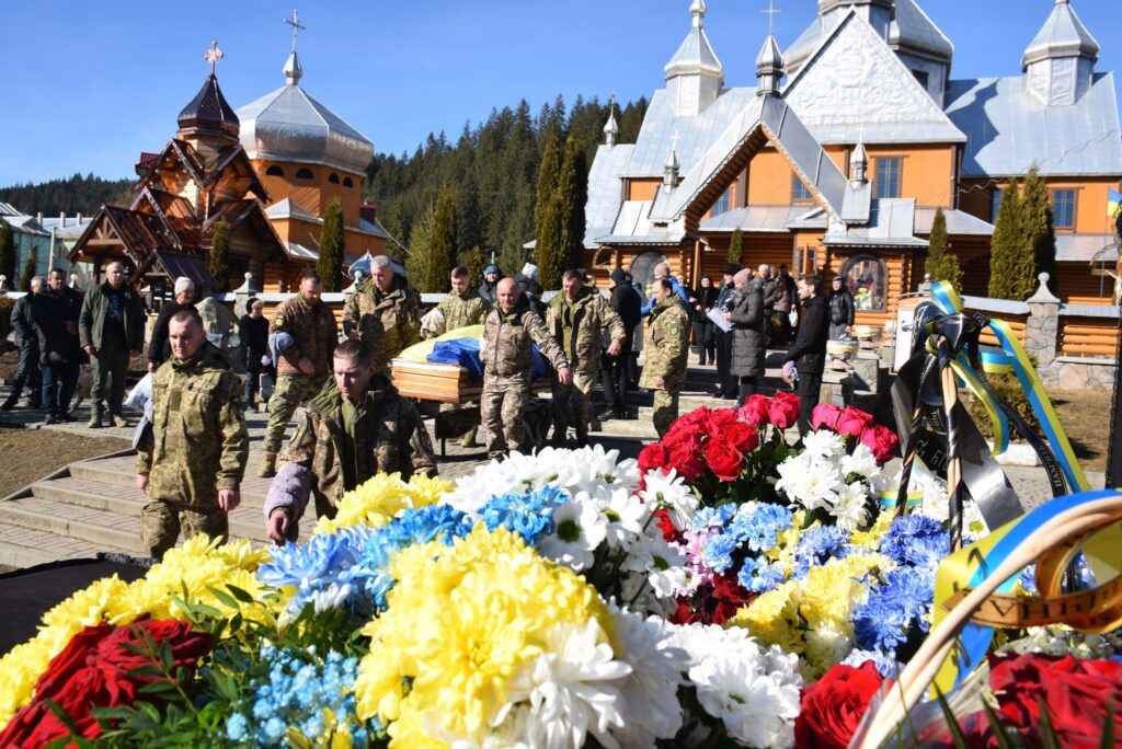 Церемонія вшанування, військові несуть труну з квітами.