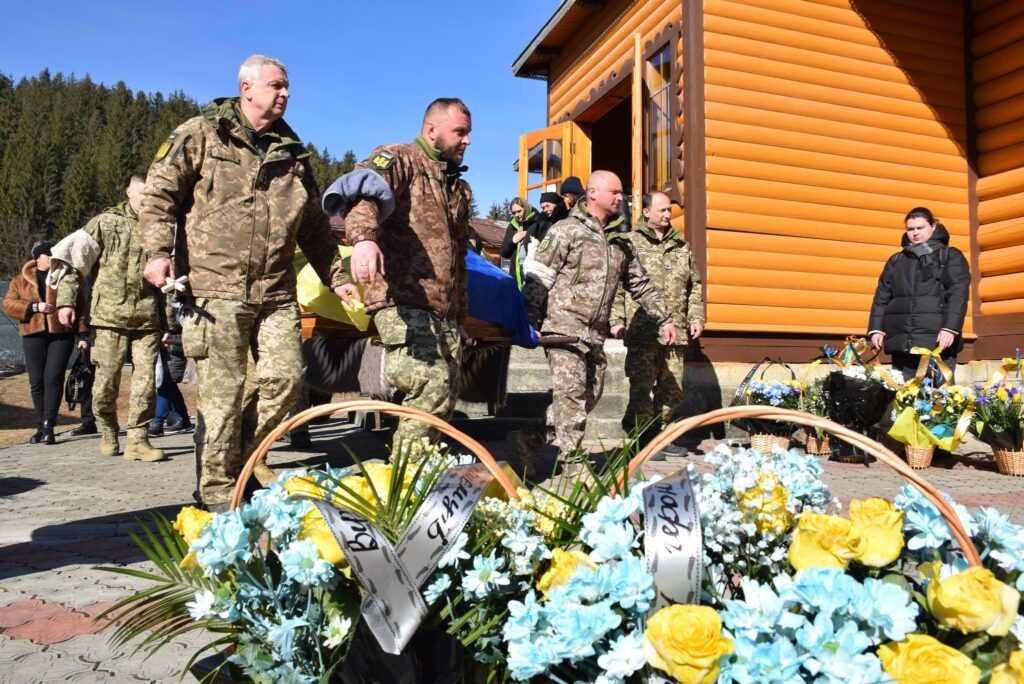 Військові несуть труну, в оточенні квітів.