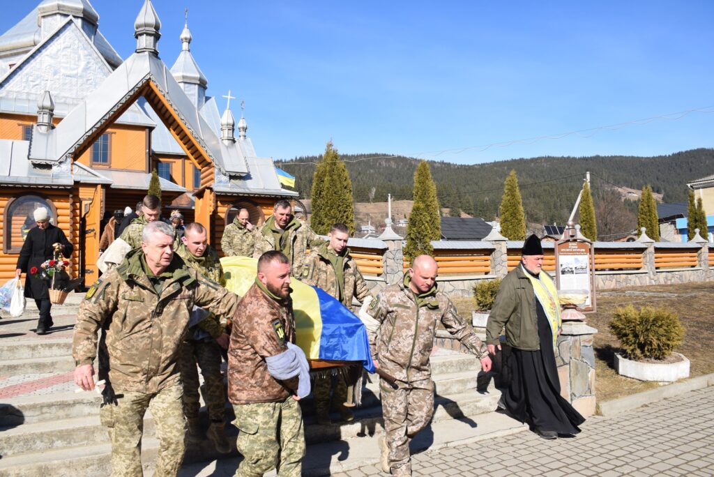 Українські військові несуть труну з прапором біля церкви.