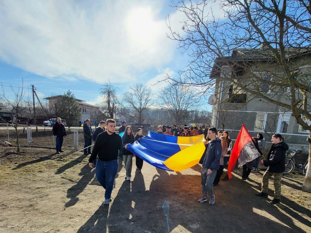 Люди несуть великий український прапор на вулиці.