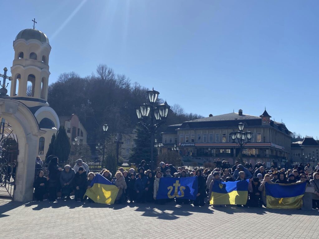 Група людей з українськими прапорами біля церкви.