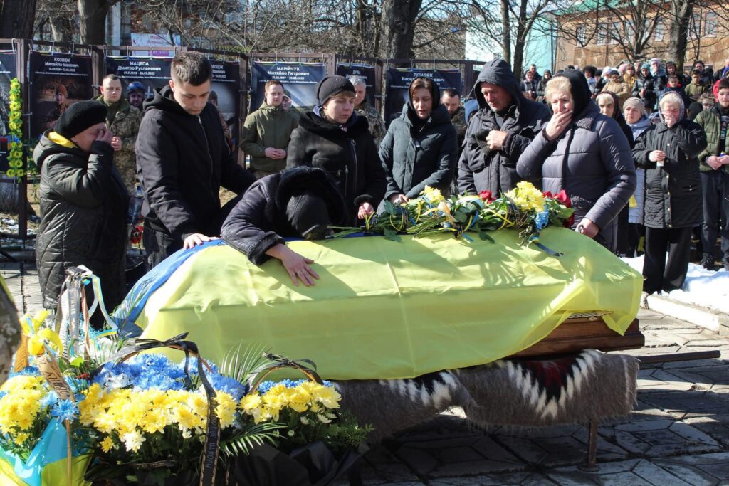 Прощання з героєм під національним прапором, родина плаче.