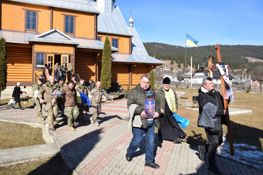 Військові несуть труну з українським прапором біля церкви