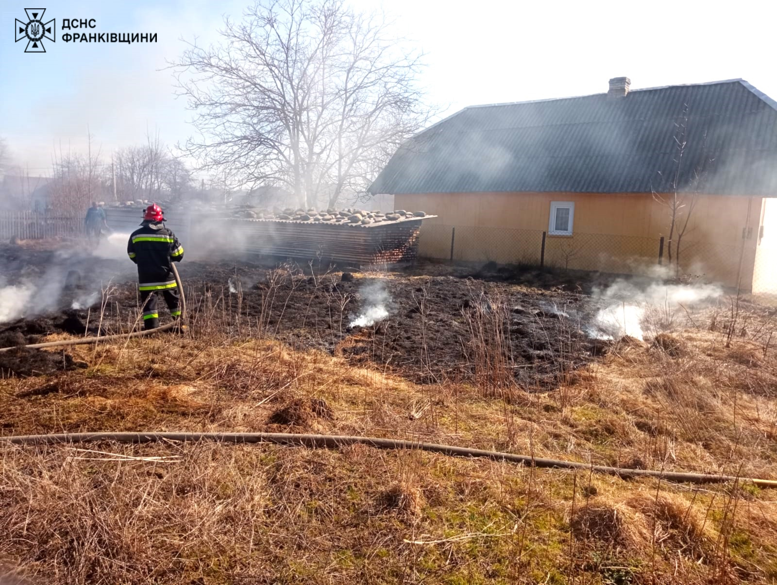 Пожежник гасить вогонь біля будинку