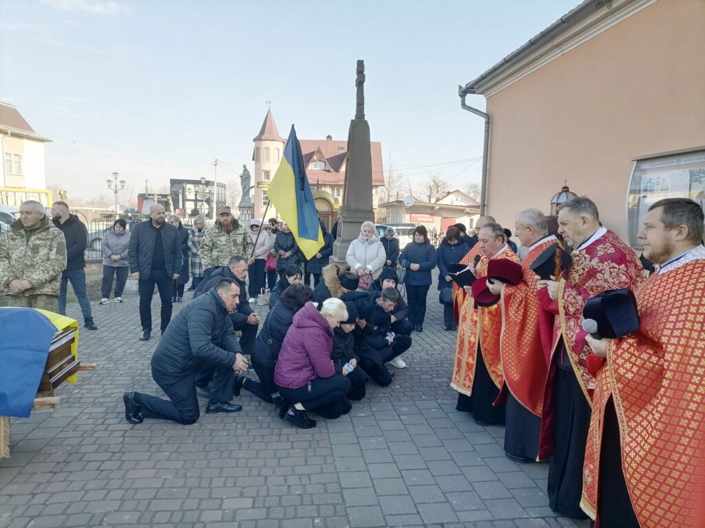 Люди на колінах біля священиків та труни.