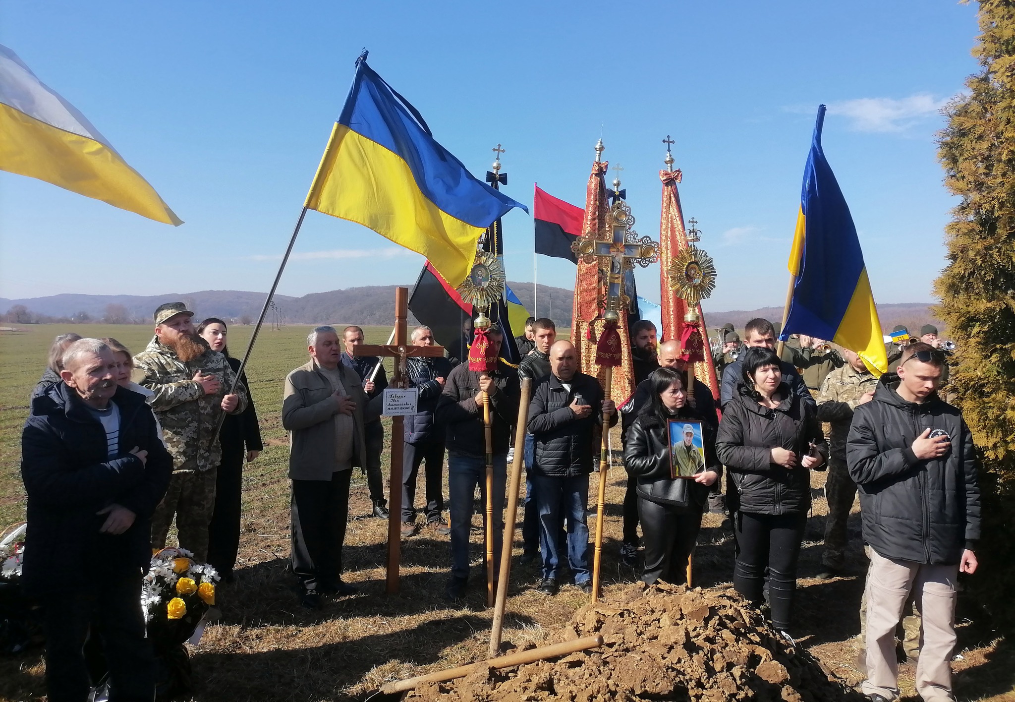 Люди на полі з українськими прапорами під час заходу.