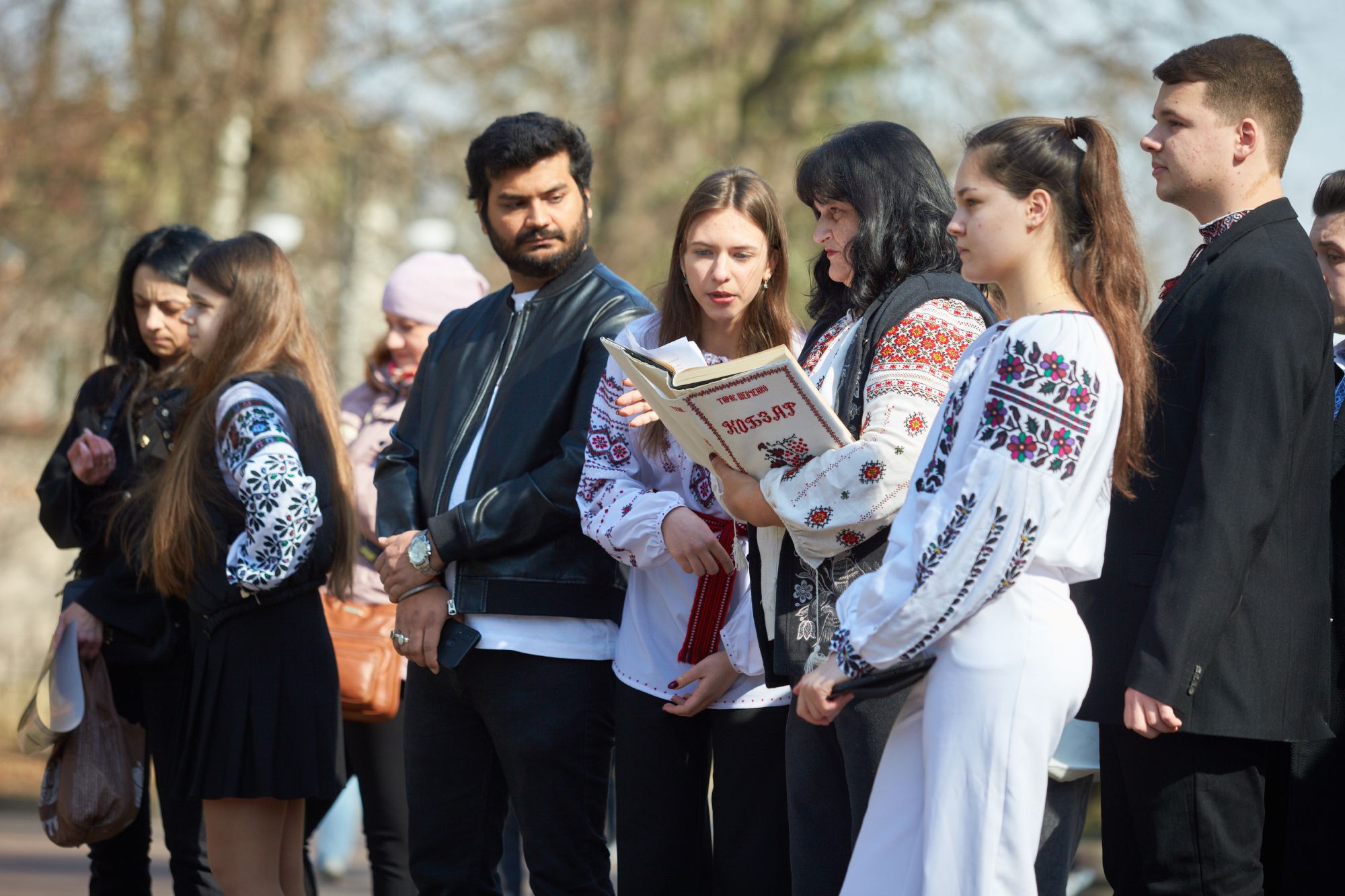 Група людей у вишиванках читає книгу на вулиці.