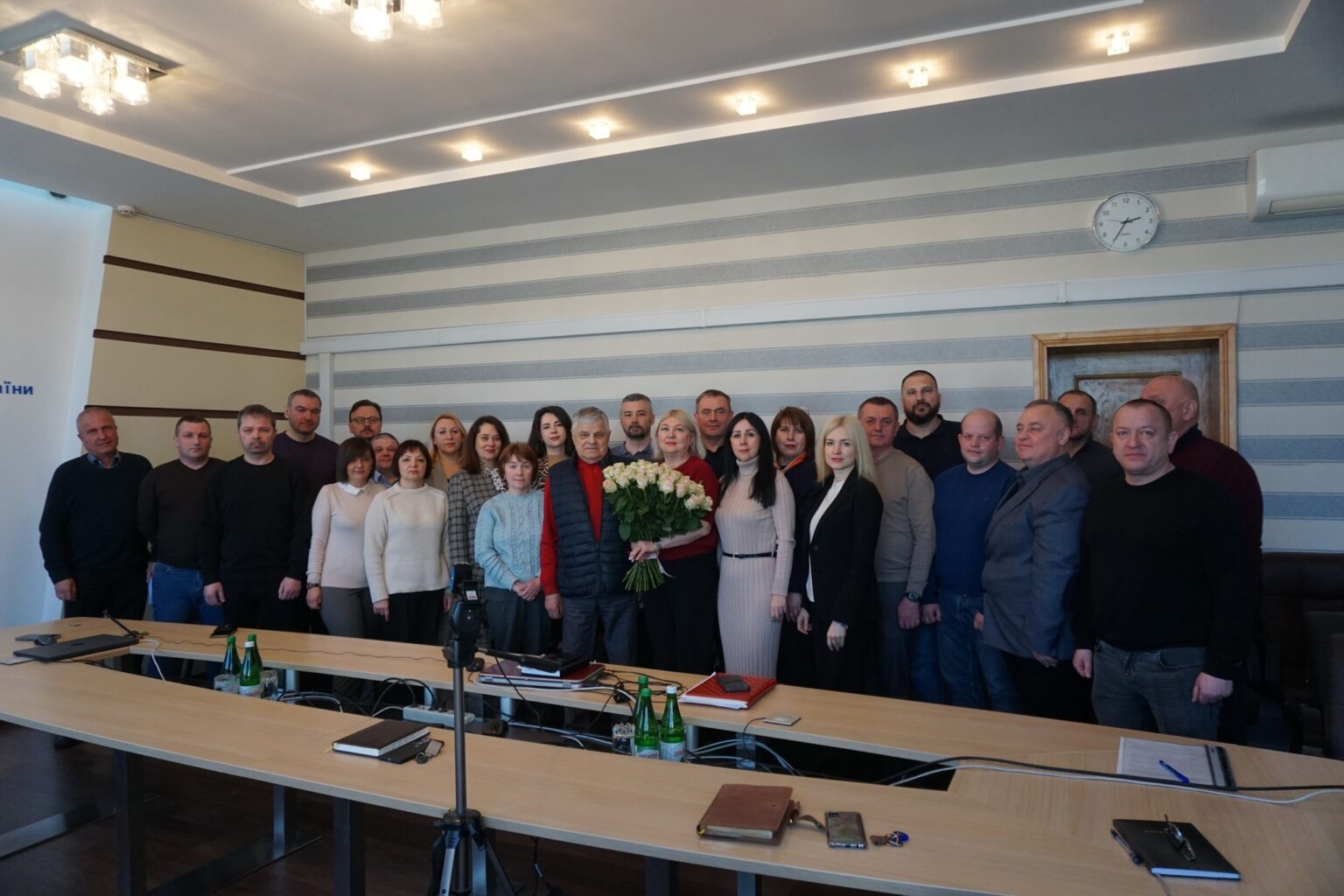 Групове фото людей в приміщенні з квітами.