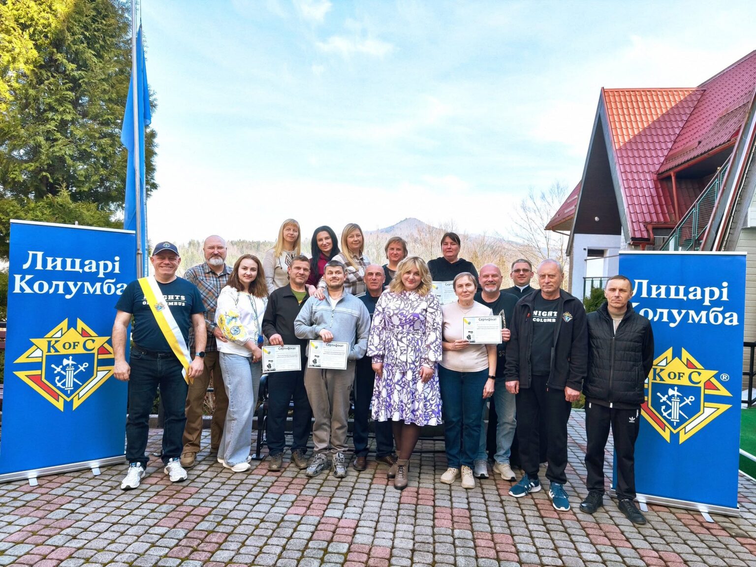 Група людей з сертифікатами біля знаків Лицарі Колумба.