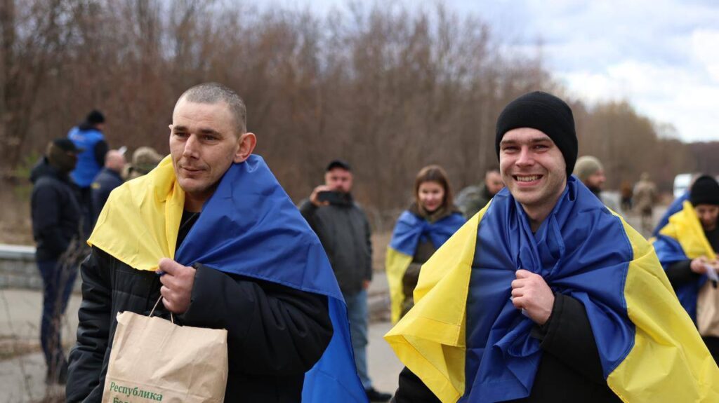 Люди загорнуті в українські прапори під відкритим небом.