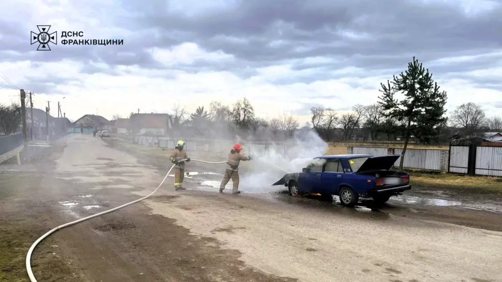 Пожежники гасять палаючий автомобіль на вулиці.