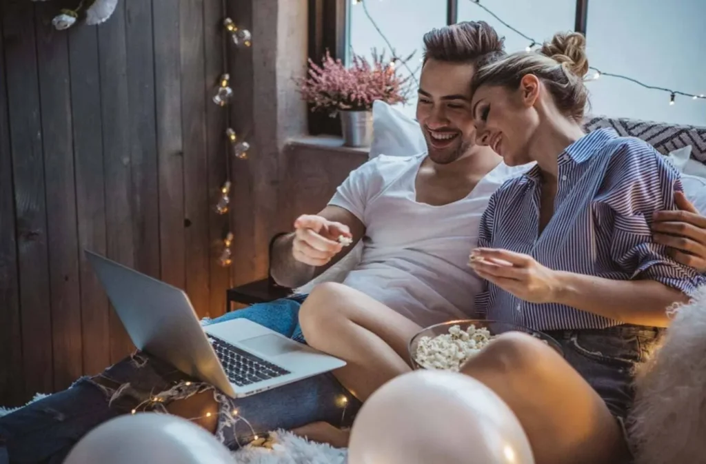 Пара дивиться фільм з ноутбуком і попкорном.
