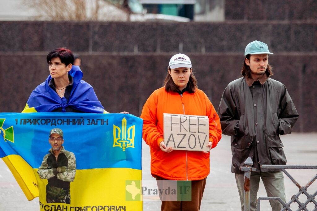 Люди тримають український прапор та плакат 'FREE AZOV'.