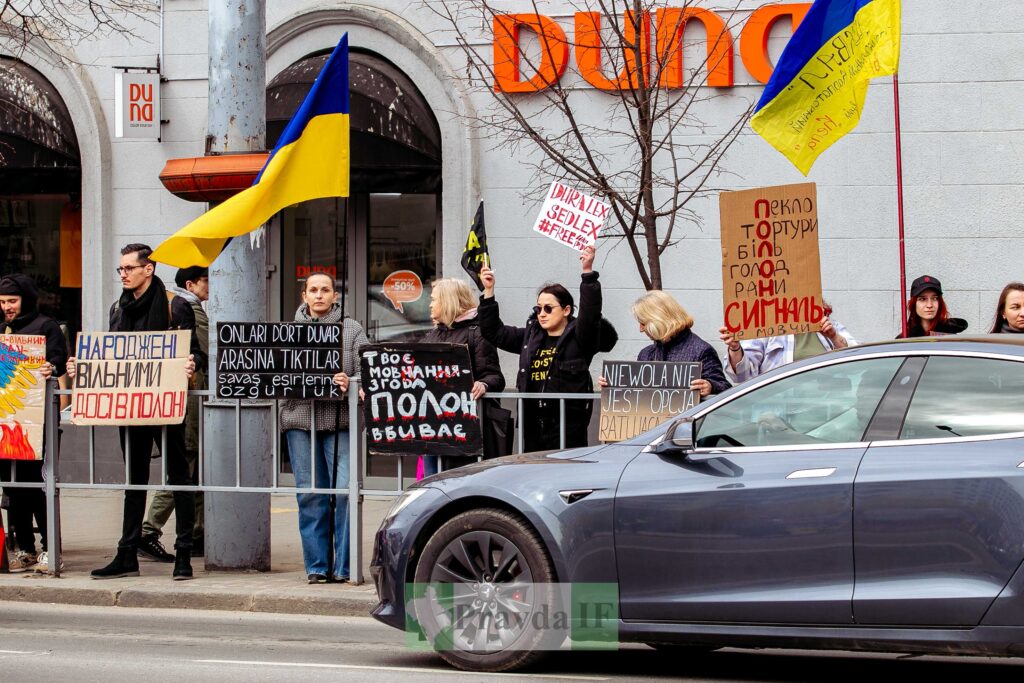 Люди з українськими прапорами на протесті біля дороги.