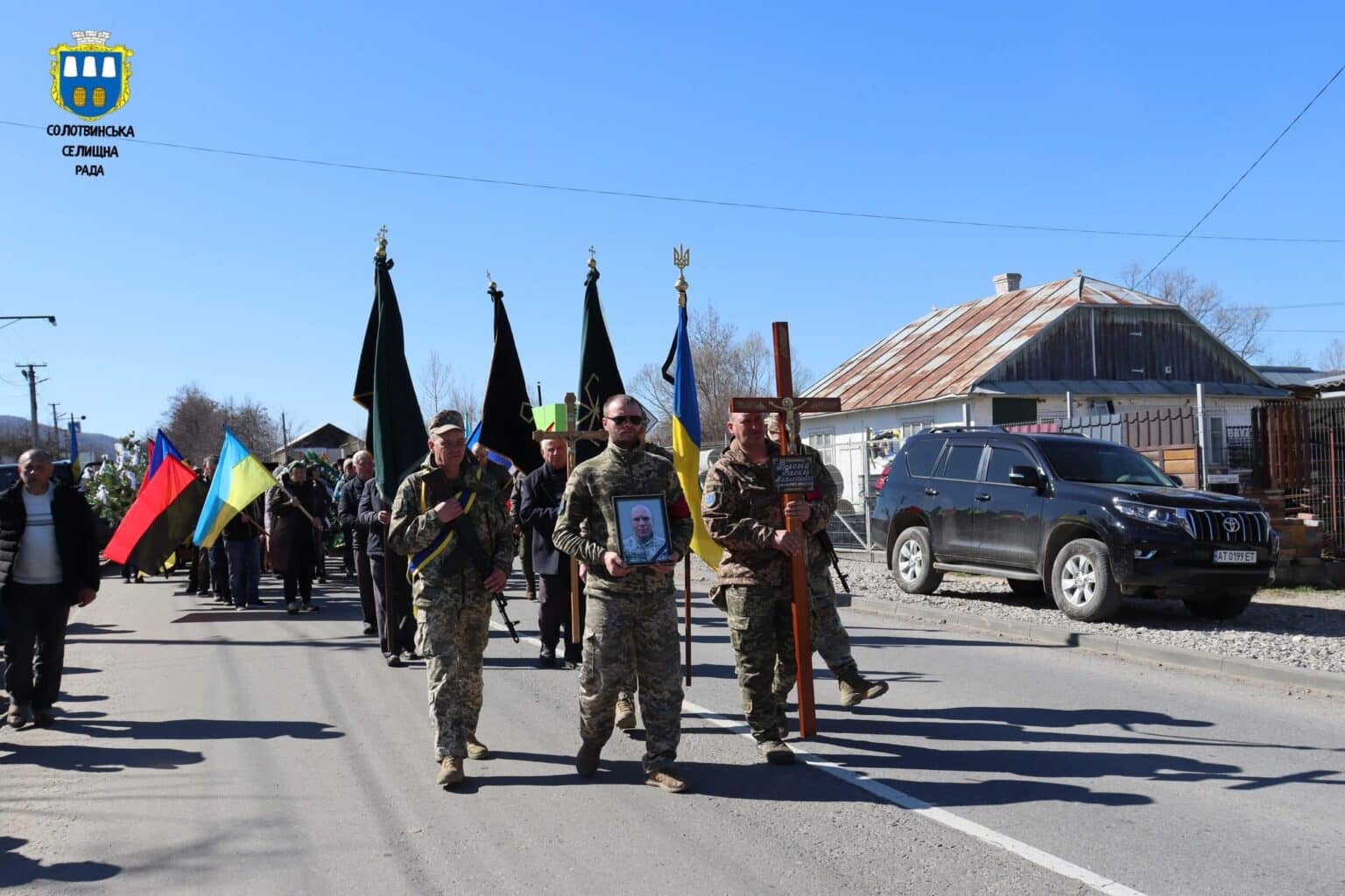 Похоронна процесія з прапорами в українському селі.