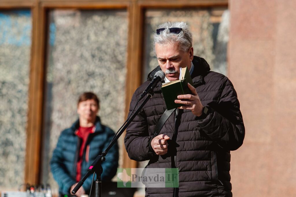 Чоловік читає з книги на мікрофоні на вулиці.