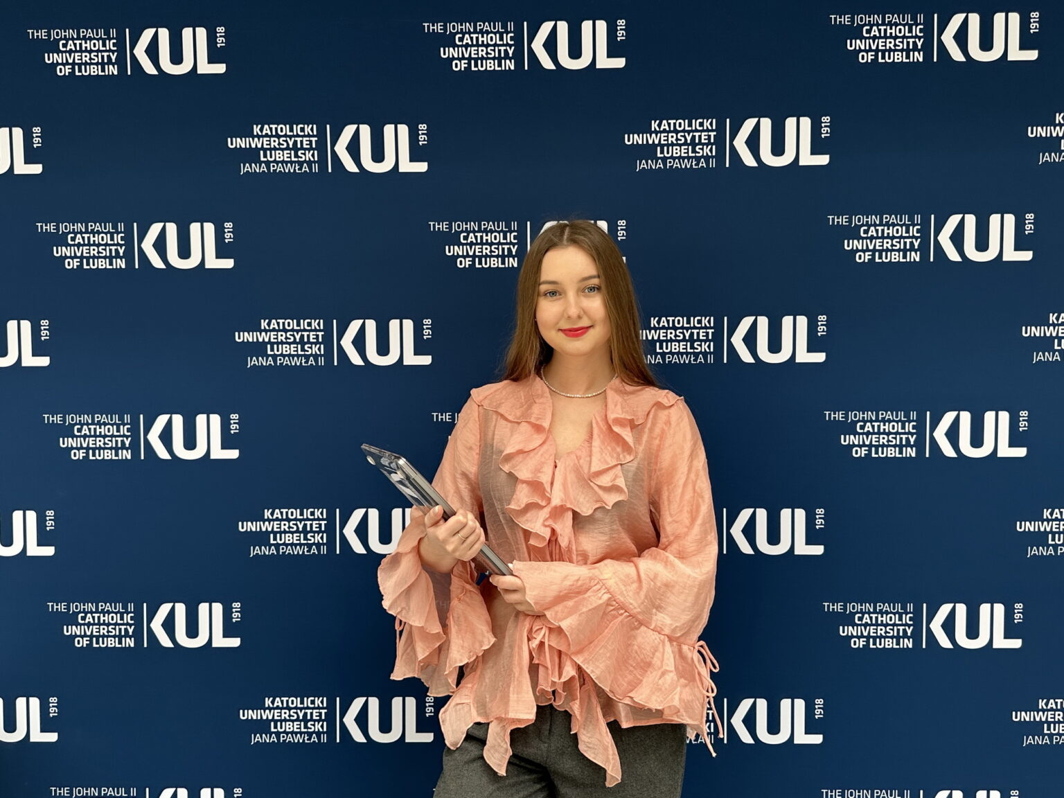 Жінка з нагородою на фоні логотипу університету