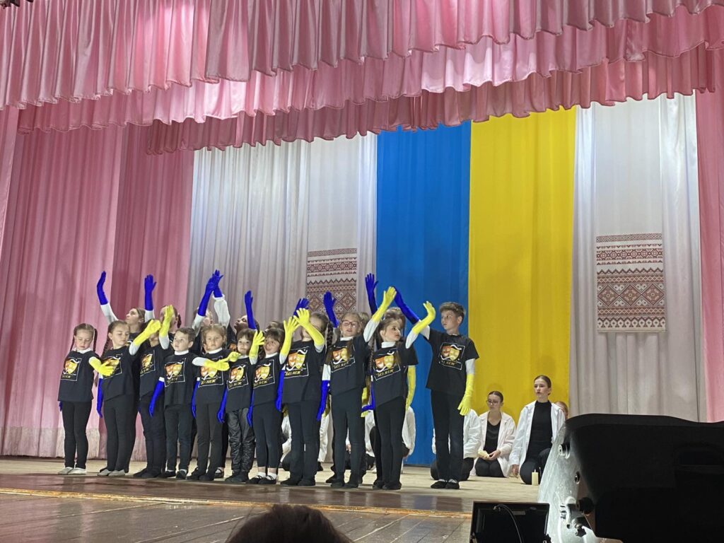 Діти виступають на сцені у жовто-синіх рукавицях.