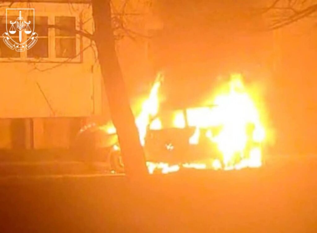 Автомобіль у вогні біля будівлі вночі.