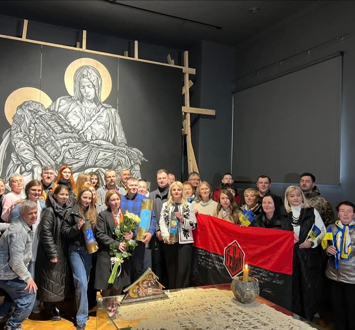 Група людей з прапорами перед іконою.