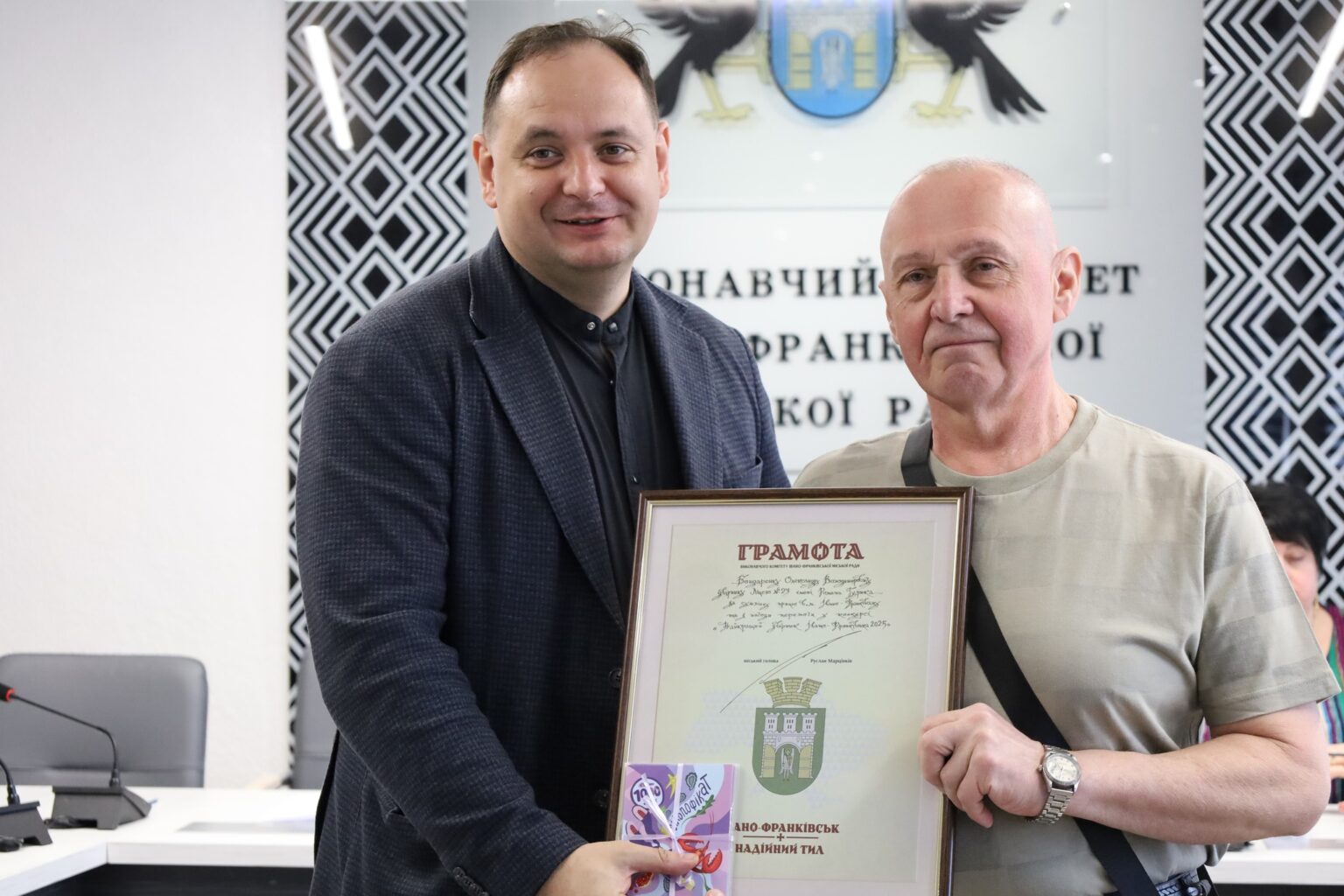 Двоє чоловіків тримають грамоту у приміщенні.