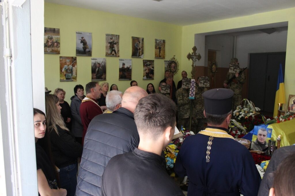 Люди зібрались на поховання у кімнаті.