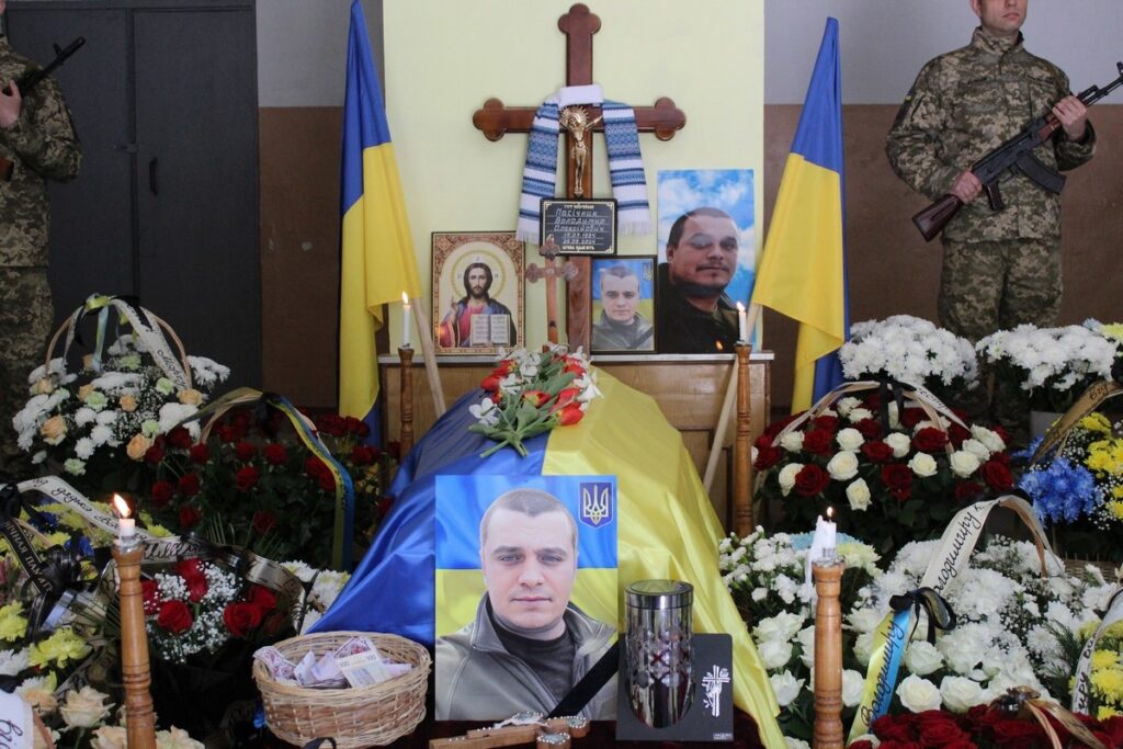 Військовий похорон з квітами та прапором України.