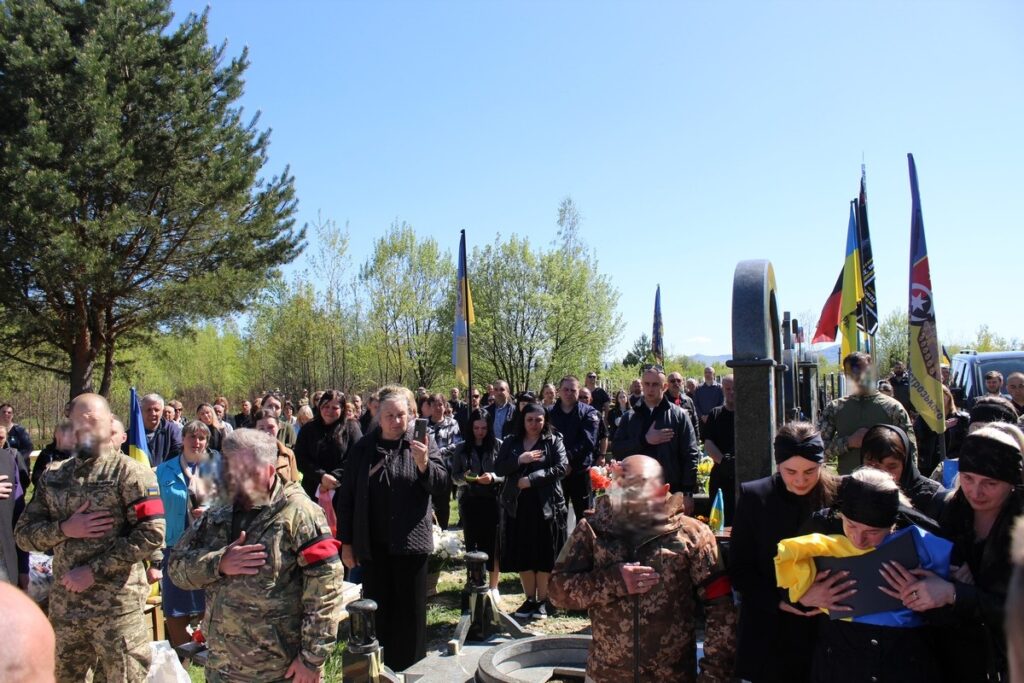 Люди на похороні, прапори, сонячний день.